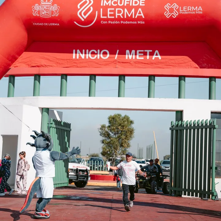 Un coureur franchit une arche d’arrivée encouragé par une mascotte
